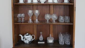 A wooden china cabinet with multiple shelves holding various white ceramic tea sets, glassware, and a decorative teapot.