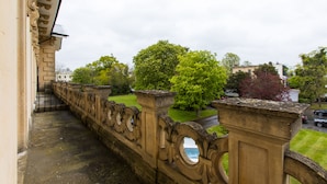 A stone balustrade with ornate carvings, a grassy lawn, and trees in the background.