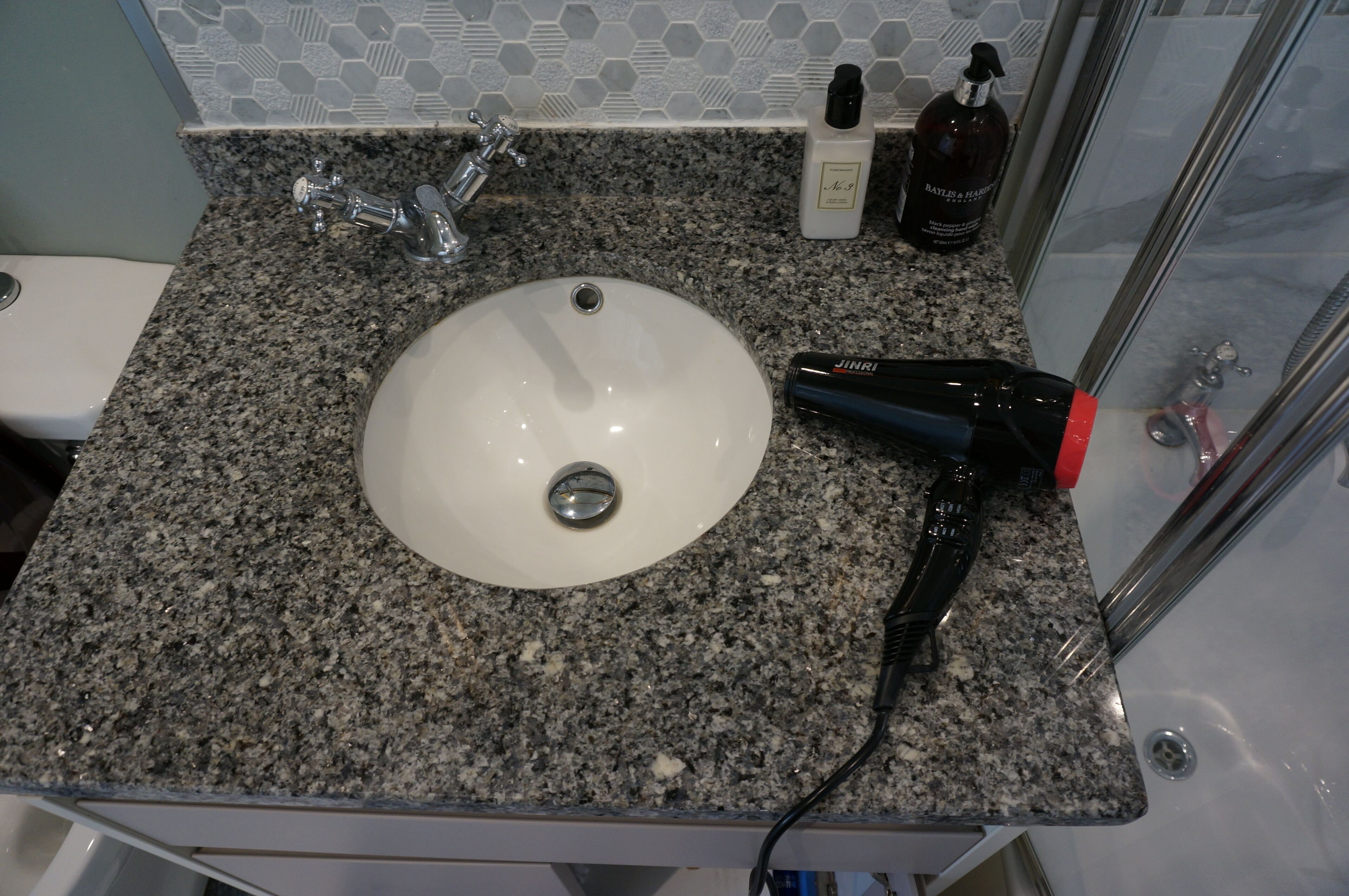 Ein Badezimmer mit einer Granitplatte, einem weißen Waschbecken, einem Handtrockner und Pflegeprodukten auf der Ablagefläche.