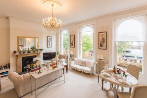 A spacious living room with a fireplace, comfortable seating, a dining area, and large windows offering a view of the outdoors. - Beautiful & spacious Regency apt in centre Cheltenham, free parking (Cheltenham)