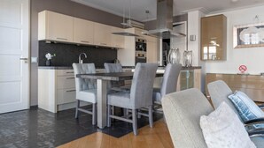A modern kitchen with a dining area, featuring a central island, grey upholstered chairs, and a large window.