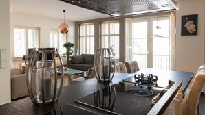 A modern kitchen with a black induction cooktop, a stainless steel range hood, and a dining area with a glass table and chairs.
