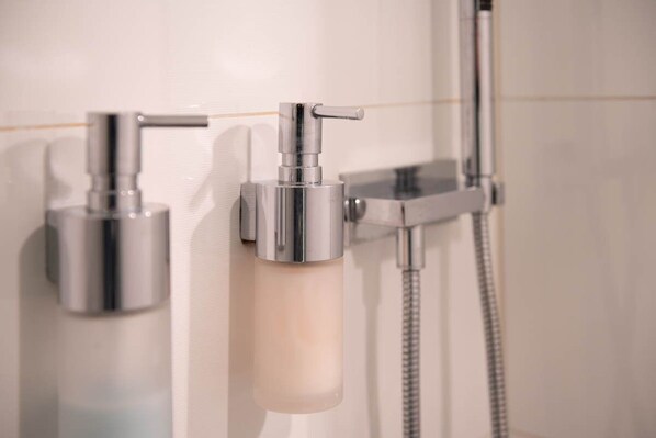 Une salle de bain équipée d’une douche, d’un distributeur de savon et d’un pommeau de douche à main.