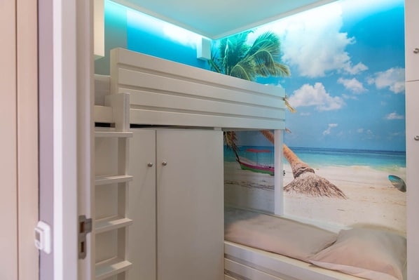 Une chambre avec un lit superposé, une armoire et une fresque murale représentant une scène de plage.