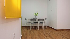 Quarto com piso de madeira, uma mesa branca com quatro cadeiras e um vaso de planta sobre a mesa.