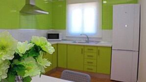 Uma cozinha com armários verdes, uma geladeira branca, um micro-ondas e uma janela com persianas.