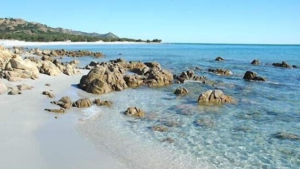 A beach with clear shallow waters and large rocks.