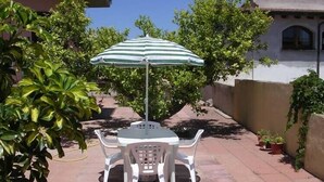 A patio with a round table and four chairs, an umbrella, and potted plants.