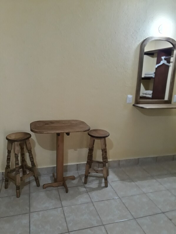 Una habitación con una mesa de madera y dos taburetes, un espejo en la pared y suelo de baldosas.