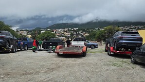 A parking lot with several vehicles, including a flatbed trailer, and a distant view of a town with buildings and hills. - Hotel Villa Aurora (Ezequiel Montes)