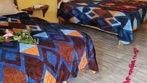 Two beds with patterned quilts, a wooden headboard, a bedside table with a book, and a rose petal trail on the floor. - Hotel Villa Aurora (Ezequiel Montes)