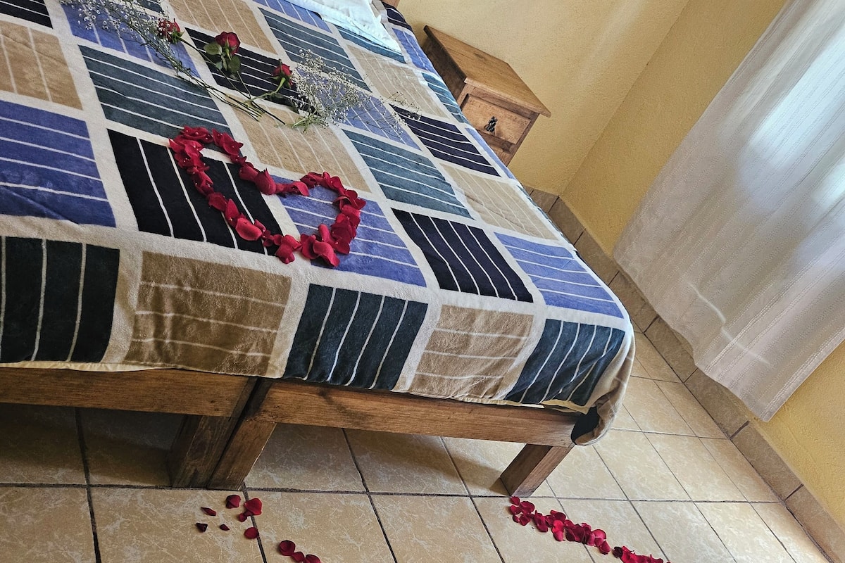 A bed with a quilt, a wooden headboard, and a small wooden nightstand beside it.