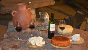 A rustic outdoor setting with a stone table displaying a bottle of wine, two glasses of red wine, a cheese wheel, and a large clay jug. - Hotel Villa Aurora (Ezequiel Montes)