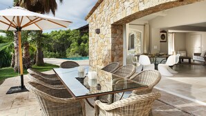 A glass-top dining table with wicker chairs, a white umbrella, and a stone wall. - Provencal villa in unique natural and calm setting with beautiful views (Fayence)