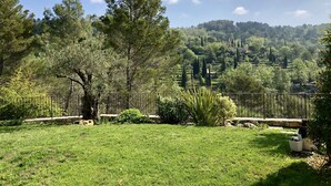 A grassy outdoor area with a stone pathway, surrounded by trees and a stone wall. - Provencal villa in unique natural and calm setting with beautiful views (Fayence)