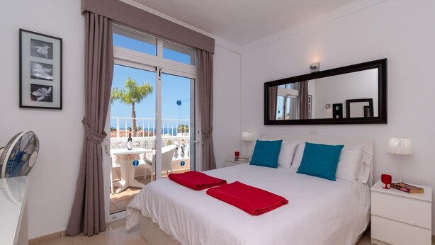 A hotel room with a bed, a large window, a fan, and a view of the beach. - .."Beautiful luxury spacious 4 bed villa Costa Adeje with a heating pool".. (COSTA ADEJE)