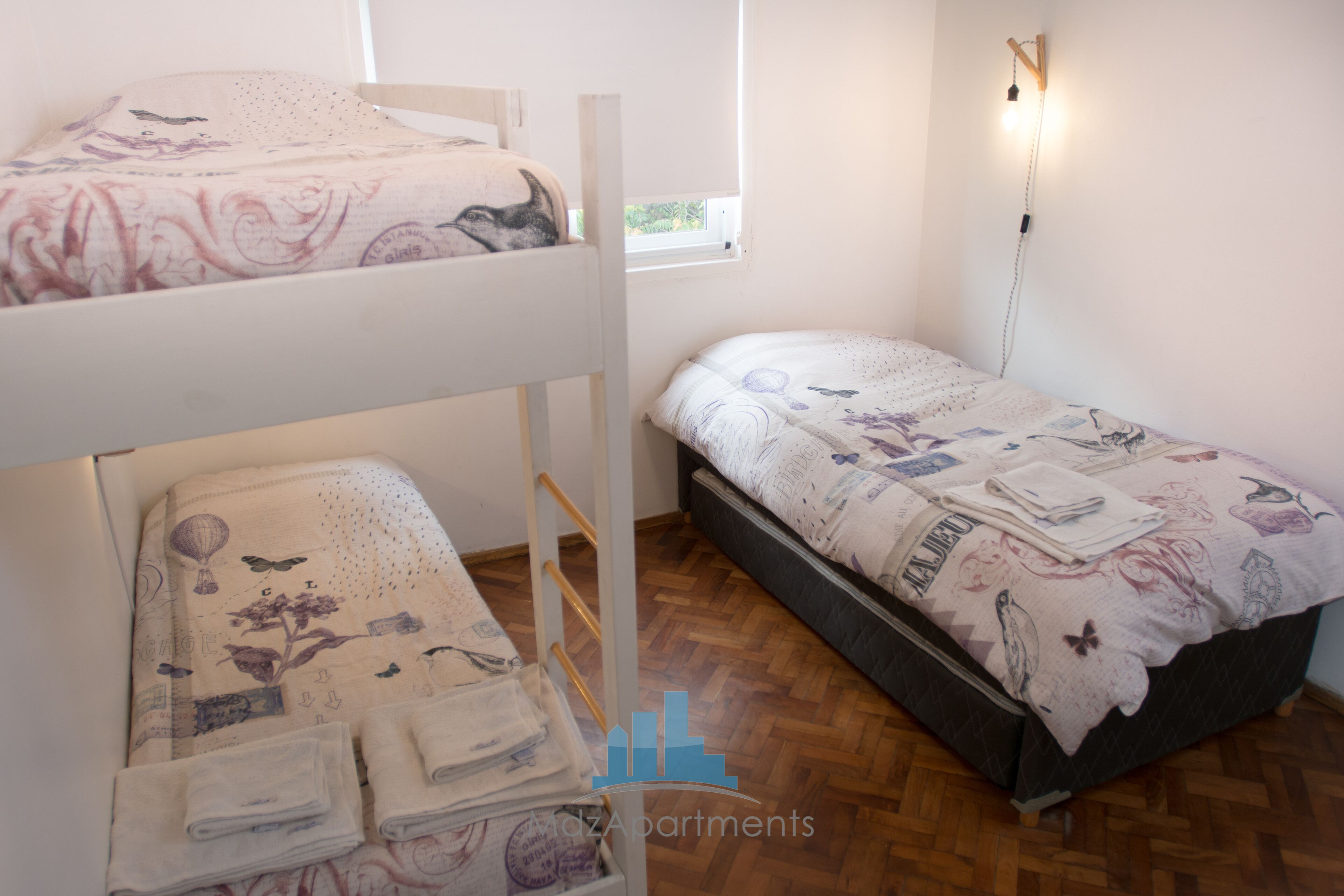 A bedroom with two bunk beds, a single bed, and a window with a view of greenery.