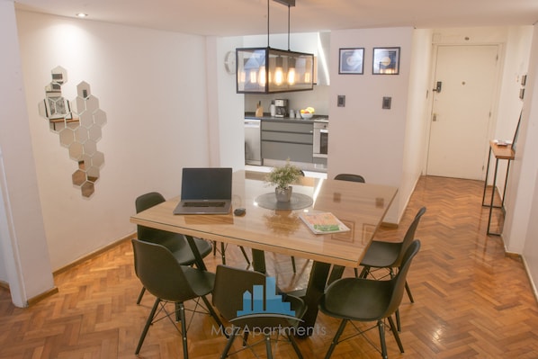 A dining area with a glass table, black chairs, a laptop, and a potted plant.