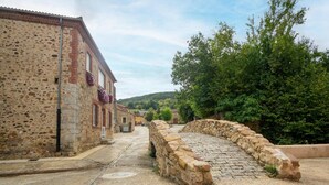 A stone bridge in a rural village with stone buildings and greenery in the background. - Tranquil Stay Near Luna River (Benllera, Carrocera, León)