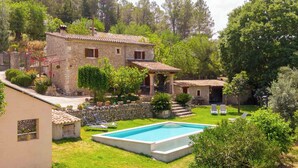 A stone house with a swimming pool, surrounded by lush greenery and a small patio area.