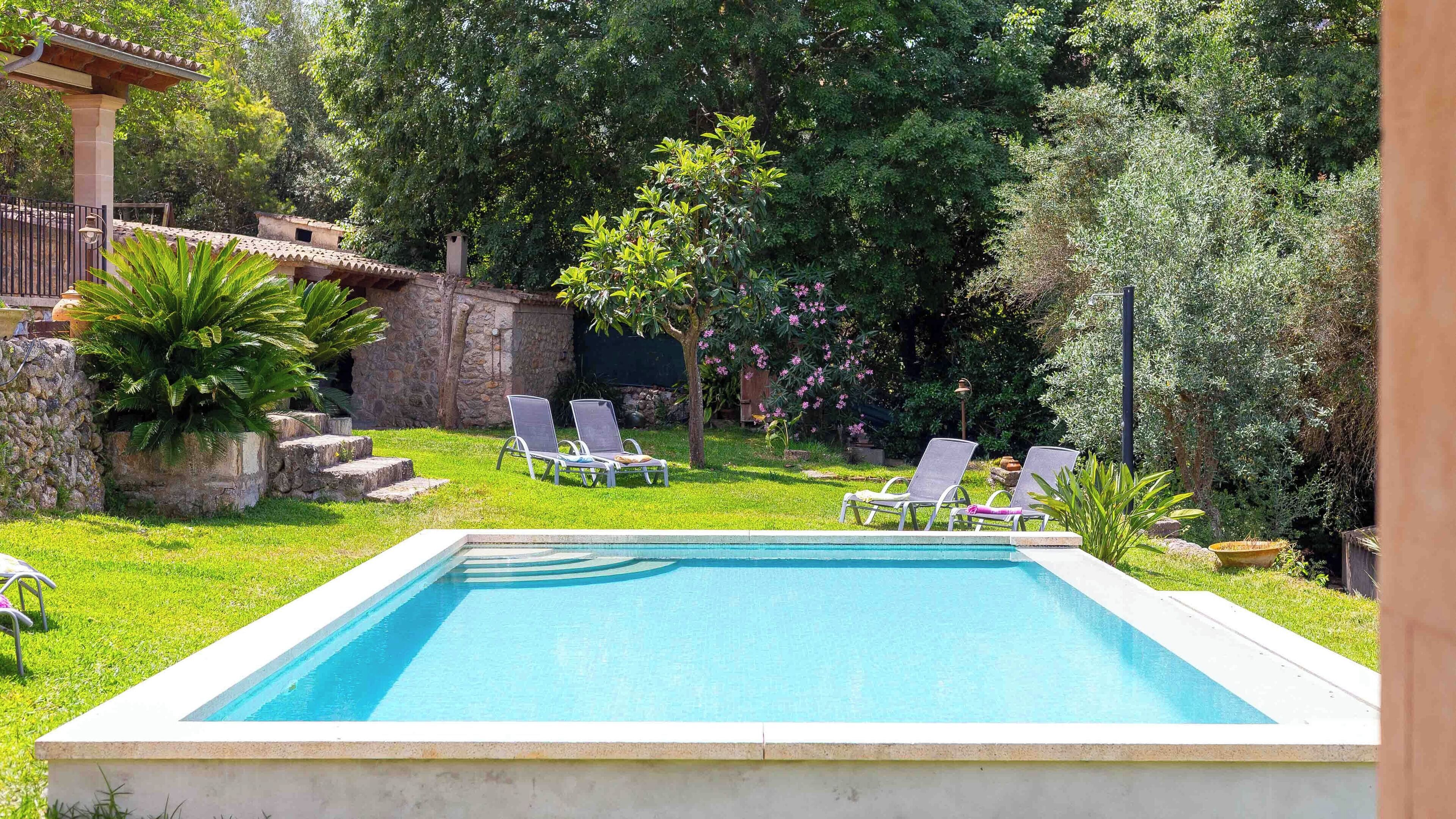 A rectangular swimming pool with two lounge chairs and a stone wall in the background.