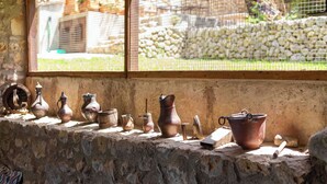 A row of rustic pottery on a stone ledge by a window with a view of a stone wall and greenery.