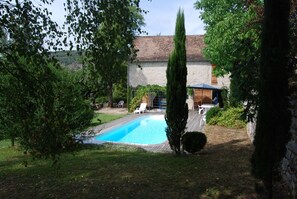 Ein Garten mit Swimmingpool, einer Holzterrasse und einem Steinhaus.