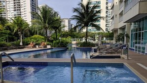 A swimming pool with a tiled edge, surrounded by palm trees and lounge chairs.