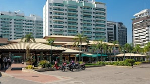 A hotel with multiple high-rise buildings, outdoor seating areas, and a paved plaza with parked scooters.