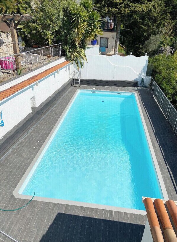 A rectangular swimming pool with clear blue water, surrounded by a white wall and a wooden deck.