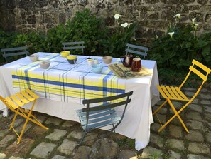 An outdoor dining area with a table set for four, surrounded by chairs, and a stone wall in the background. - Le Logis des Abbesses - A hanging garden on the Loire. (Montsoreau)
