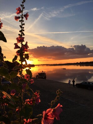 Ein Sonnenuntergang über einem ruhigen See mit Booten und Menschen am Ufer.