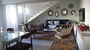 Ein modernes Wohnzimmer mit einem Glastisch, bequemen Sitzgelegenheiten, einer Treppe und dekorativen Wandspiegeln.