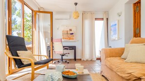 A modern living room with a wooden chair, a sofa, a dining table with a decorative elephant, and a view through large windows. - Cubo's Casa Lucia Private Pool / Wifi / Air conditioning / private garden / BBQ (Alhaurín el Grande)
