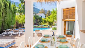A poolside dining area with a table set for four, surrounded by lounge chairs and a view of a mountain landscape. - Cubo's Casa Lucia Private Pool / Wifi / Air conditioning / private garden / BBQ (Alhaurín el Grande)