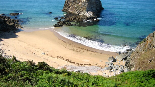 A beach with clear blue water, a large rock formation, and a sandy shore.
