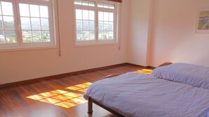 A bedroom with a wooden floor, two beds, and large windows with a view of a landscape.