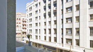 Ein Balkon mit kleinem Tisch und einer Topfpflanze, mit Blick auf ein mehrstöckiges Gebäude mit Balkonen.