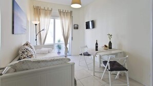 Ein modernes, gut beleuchtetes Zimmer mit einem Bett, einem Esstisch mit Stühlen, einem an der Wand befestigten Fernseher und einem Fenster mit Vorhängen.