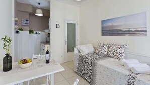 Ein gemütlicher Raum mit einem Bett, einem Esstisch mit Obstschale und Wein, einer kleinen Küchenzeile und einem Bild an der Wand.