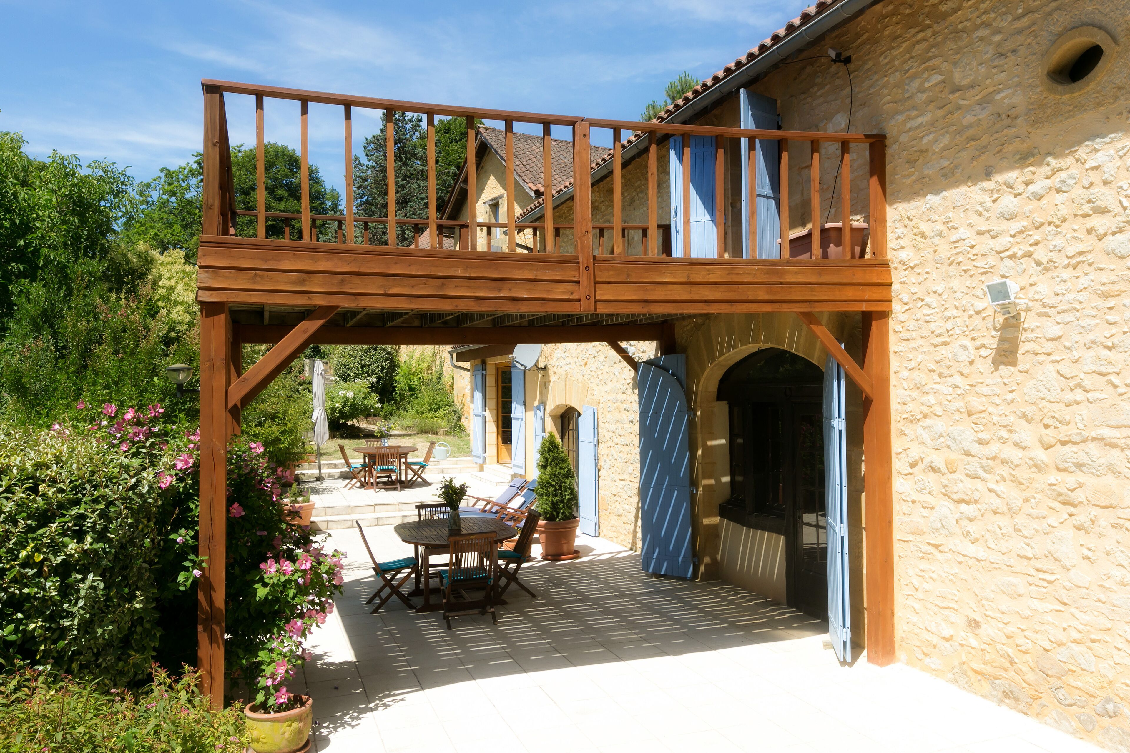 A wooden deck with a table and chairs, a stone building with a window, and a potted plant.