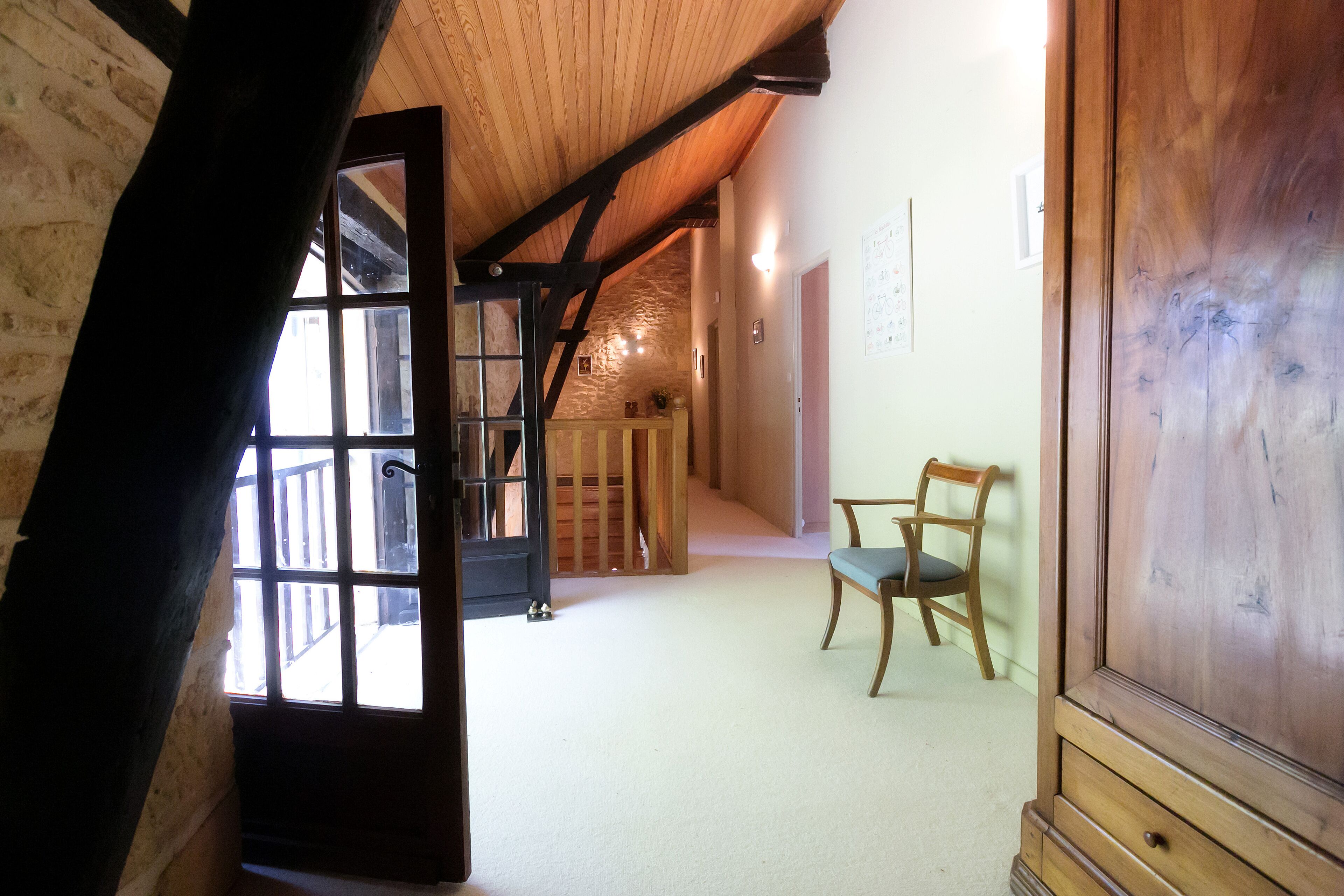 Un couloir avec une chaise en bois, un meuble en bois et un escalier menant à l’étage supérieur.