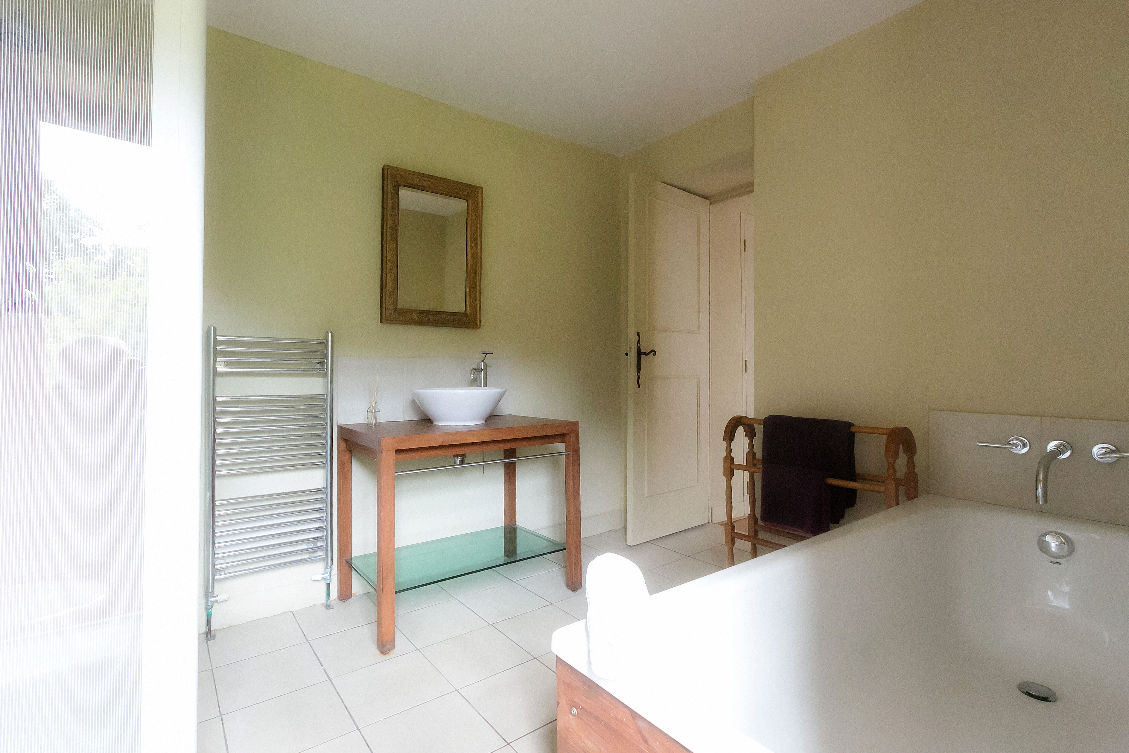 A bathroom with a bathtub, a sink, a mirror, and a door.