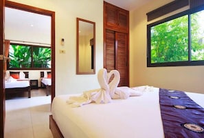 Habitación de hotel con cama, espejo, ventana con vistas a vegetación y puerta que da a otra habitación.