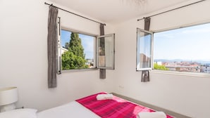A hotel room with a bed, a window with curtains, and a view of buildings and trees.