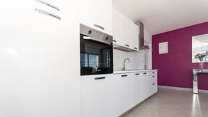 A modern kitchen with white cabinets, a black oven, and a purple accent wall.