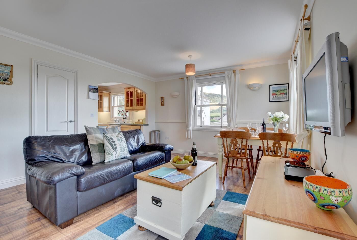 A cozy living room with a leather sofa, a small white coffee table, and a dining area with wooden chairs and a table.