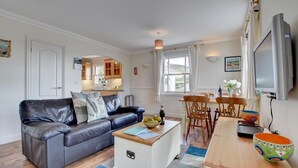 A cozy living room with a leather sofa, a small white coffee table, and a dining area with wooden chairs and a table. - 2 Bed in Woolacombe (oc-goldbe) (Woolacombe)