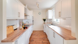 A narrow kitchen with white cabinets, wooden countertops, and a wooden floor. - 2 Bed in Woolacombe (oc-goldbe) (Woolacombe)