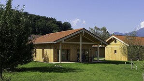 Een houten hut met een rode dakbedekking, een overdekte veranda en uitzicht op bergen op de achtergrond.